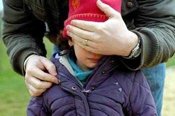 photo d'une enfant, la main d'un adulte plaquée sur ses yeux, l'autre sur la fermeture de sa veste